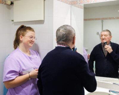 Une professionnelle de la maison en train d'accompagner un résident qui se rase